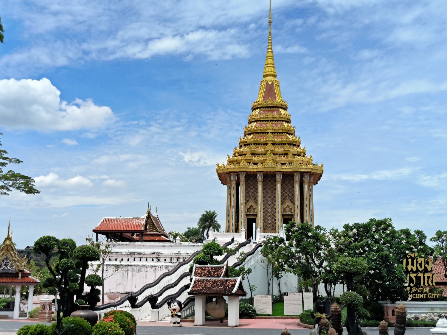 A tall temple resembling Wat Phra Phutthabat, located in the Ancient City. Its towering structure is accessed by a winding staircase, with a roof reaching toward the clear sky.